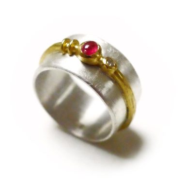 Silberner Ring mit goldener Umrandung und rotem Edelstein in der Mitte.