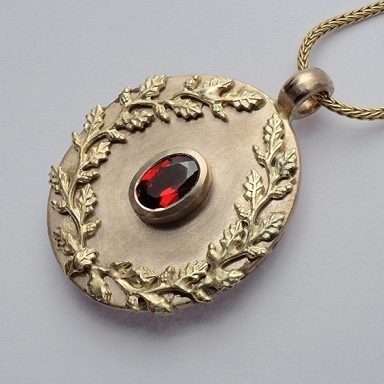 Ovaler Anhänger mit rotem Granat, umrandet von einer goldenen Blätterranke.