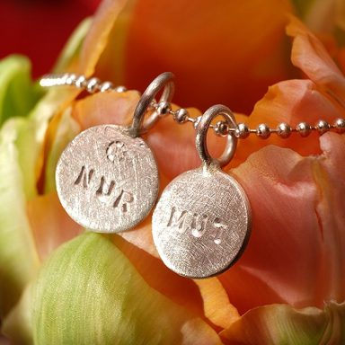 Zwei silberne Kettenanhänger beschriftet mit den Worten NUR MUT