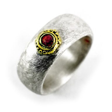 Silberner Ring mit goldener Fassung und rotem Stein in der Mitte.